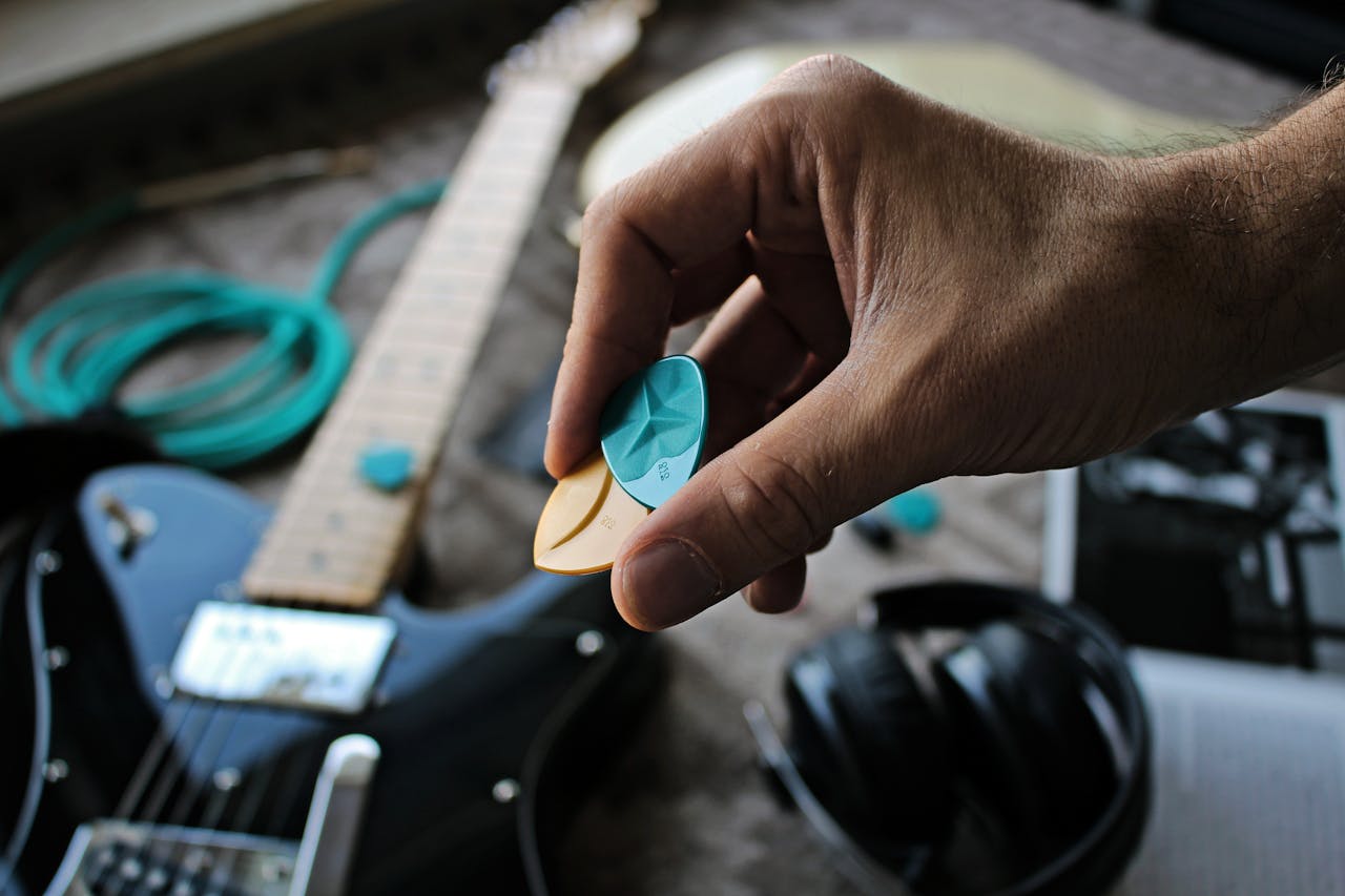 Close-up of a hand holding colorful guitar picks next to an electric guitar on a musical setup.