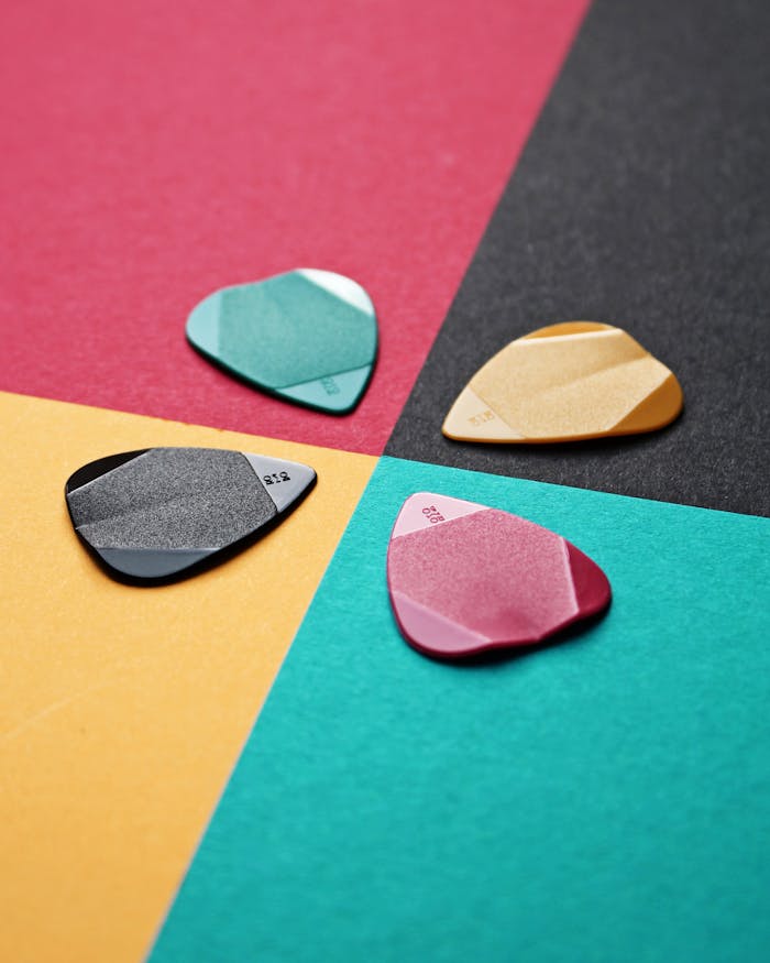Diverse guitar picks on vibrant overlapping colored paper surfaces, showcasing musical accessories.