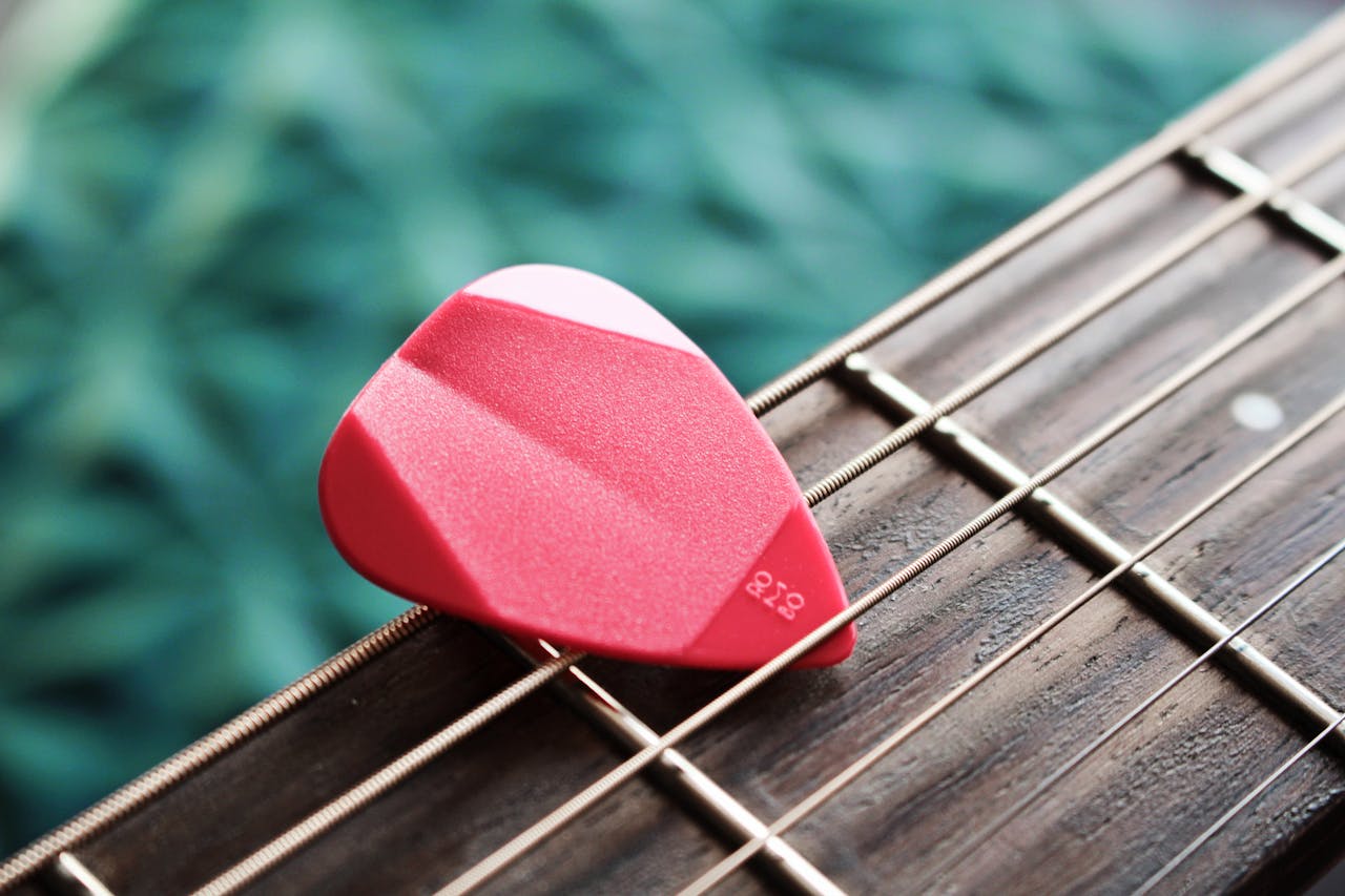 A detailed view of a red guitar pick resting on acoustic guitar strings.